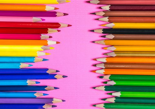 Bright colored pencils for drawing on pink background placed in two rows, top view