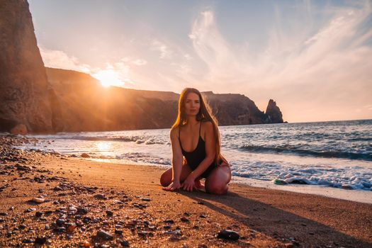 Selective focus. Happy carefree sensual woman with long hair in black swimwear posing at sunset beach. Silhouette of young beautiful playful positive woman outdoor. Summer vacation and trip concept.