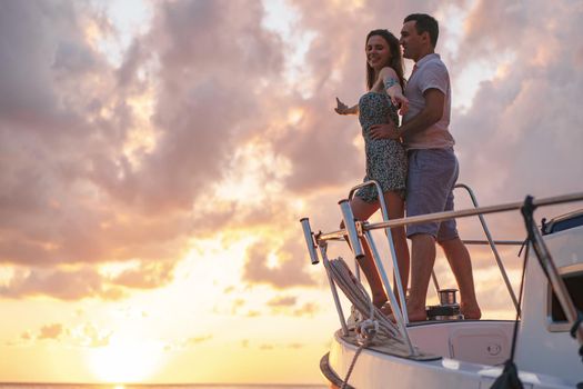 Beautiful loving couple looking at sunset from the yacht