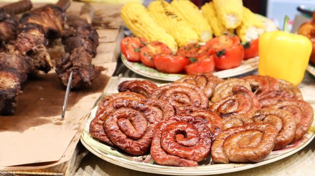 A counter with trays containing grilled sausages and meat. Round barbecue sausage street food showcase. Freshly grilled round sausages at a street food festival. A variety of meat delicacies.