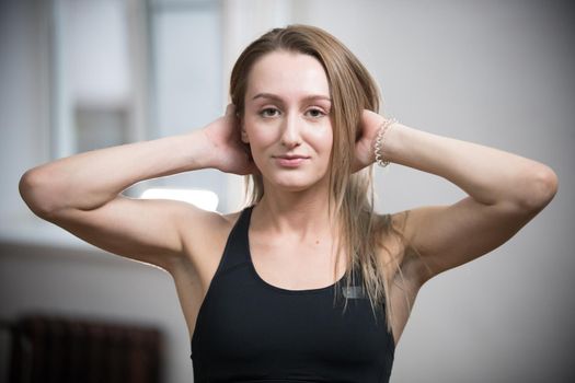 Young attractive woman in sport bra in training studio touching her hair. Portrait