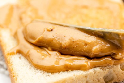 Crunchy peanut butter spreading on a toast, close up