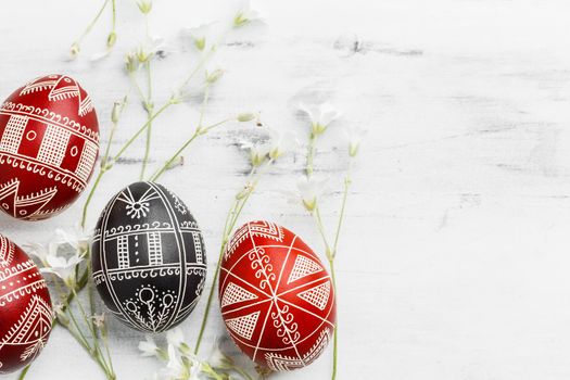 Red and black handmade Easter Pysanka eggs. Ukrainian pysanky decorated with wax-resist dyeing technique. White wooden background with copy space for text