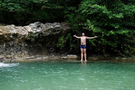 Tropical nature and vacation. Man swimming in the mountain river with a waterfall