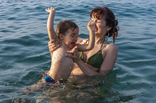 Happy family and healthy lifestyle. Young mom teaches a child to swim in the sea