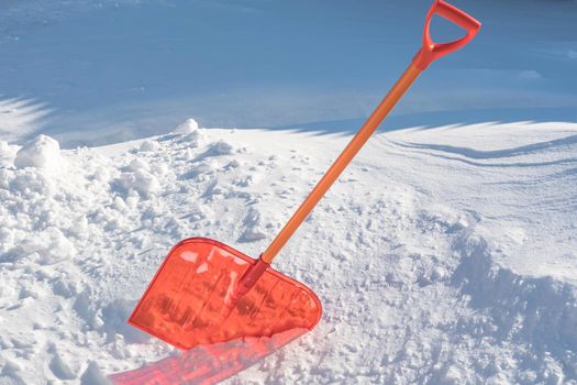 A snow shovel is stuck in a snowdrift in winter in winter. Snow removal, cleaning the street from snow drifts. A white pile of snow. Snowy weather in winter. A red shovel. Snowy Crystals