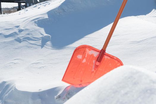 A snow shovel is stuck in a snowdrift in winter in winter. Snow removal, cleaning the street from snow drifts. A white pile of snow. Snowy frost weather in winter. A red shovel. Snowy Crystals