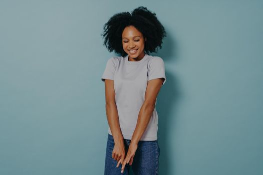Cute young african lady wearing casual outfit looking down with with shy timid face expression, shrugging shoulders and feeling embarrassed with uncomfortable question, isolated over blue background