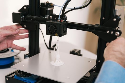 Young engineer in the lab adjusting a 3D printer's components.