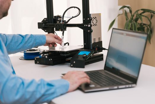 Young engineer in the lab adjusting a 3D printer's components.