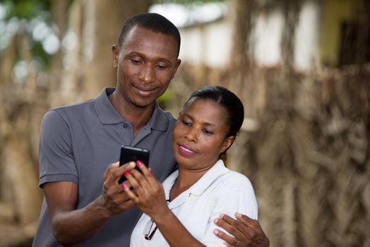 Cheerful couple embracing outdoors in the open air and watching on a mobile phone