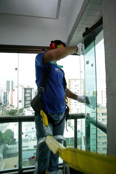 salvador, bahia, brazil - may 17, 2017: Worker wears seat belt while installing a window in a building in Salvador city.