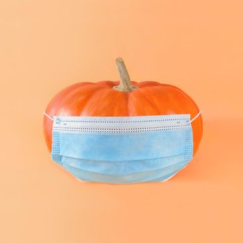 Orange pumpkin in medical mask on beige background.