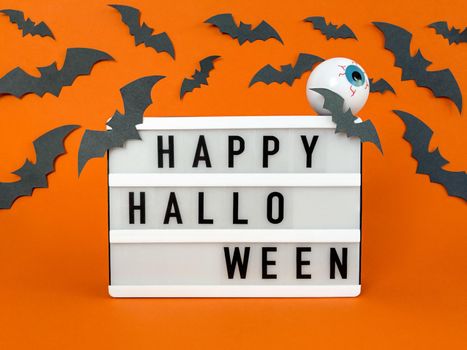 Light box with Happy Halloween phrase with bats and eyeball decoration on orange background.