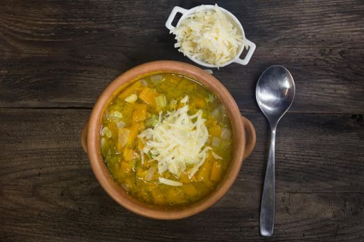 casserole with hot vegetable soup and grated cheese on rustic wood