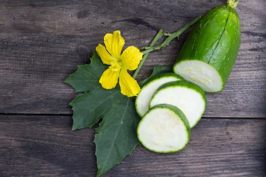 fruit and flower of the green luffa that is used for Asian cuisine, on rustic wooden background