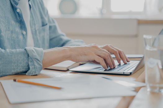 Cropped shot of man using laptop computer at home, male hands typing on keyboard on kitchen table. Closeup of technology in use and work remotely online concept