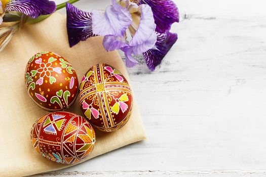 Three handmade Easter eggs decorated with wax-resist dyeing technique. Ukrainian pysanka on white shabby wooden background with empty space for text