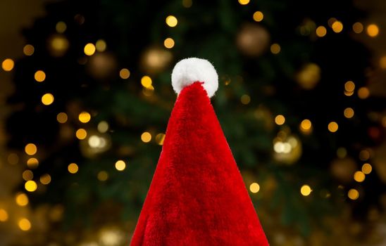 Santa hat on the background of a Christmas tree and garlands. Close-up Christmas concept red hat on bokeh background of glowing garlands