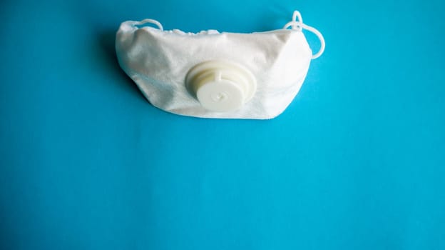 White protective medical mask with a valve on a blue background with copy space. Protective face mask against pollution, viruses, flu and coronavirus. Health care and surgical concept
