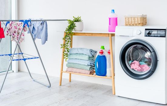 Washing machine with laundry in bathroom and furniture with detergents for cleaning and housework