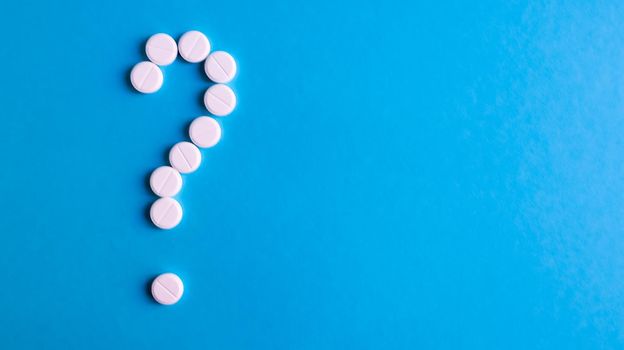 Question mark made of many white pills on a blue background. Healthcare concept. Creative medicine for health medical problem, drug interaction, medication error and pharmaceutical concept