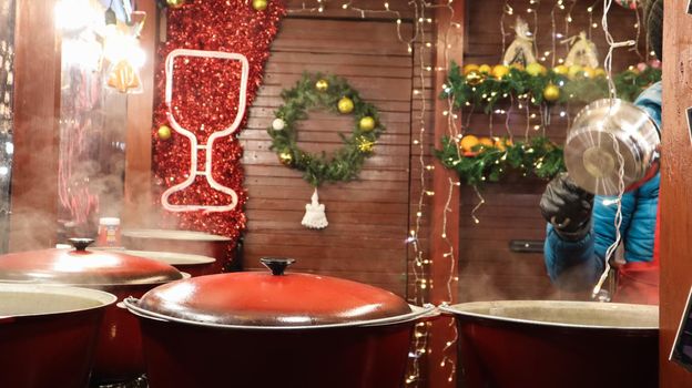 Ukraine, Kiev - January 7, 2020. Winter hot drink lintwein on a campfire on the street. Street diner at the Christmas market in winter. Hot mulled wine. Dense steam over boilers of hot wine.