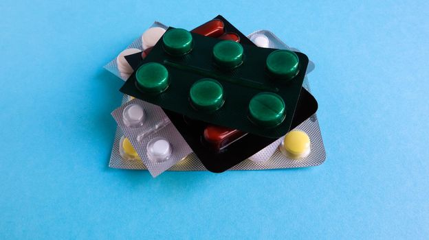 Packs of pills of various shapes and colors are stacked on a blue background. Capsules are packaged in blister packs. Different medicines. Drug treatment. Health photo. Copy space