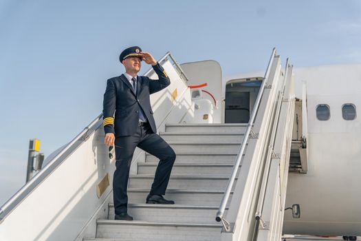Pilot holding his hand near the cap and standing on the steps of the plane. Profession concept