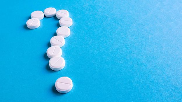 Question mark made of many white pills on a blue background. Healthcare concept. Creative medicine for health medical problem, drug interaction, medication error and pharmaceutical concept