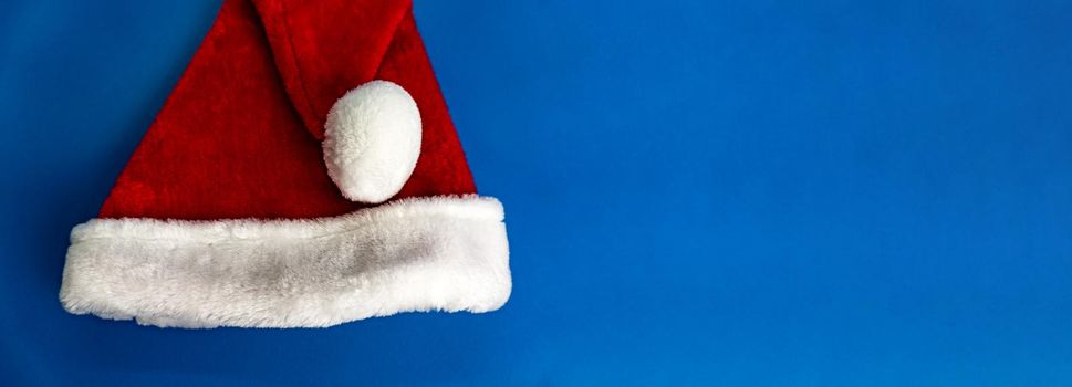 Banner of red santa clauses hat with fur on blue background, trendy color of the year 2020. Enough space for text.