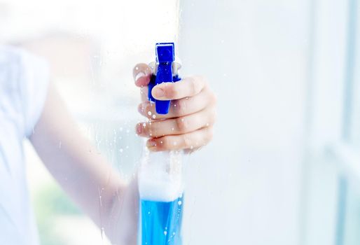 Woman hand holding bottle of blue cleaning spray, through transparent window