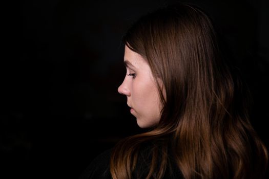 Studio black background dark black clothes portrait girl evening reception profile side brunette hair looks edge frame. Copy space left