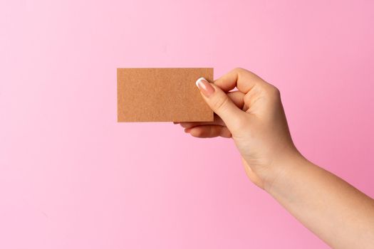 Woman hand showing blank business card on pink background. Close up.