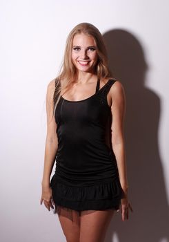 Beautiful Fashion blogirl in small black dress and very long blonde hair stay near white wall with hard shadow
