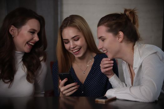 Young beautiful women sitting in a bar looking on telephone, laughing. Portrait