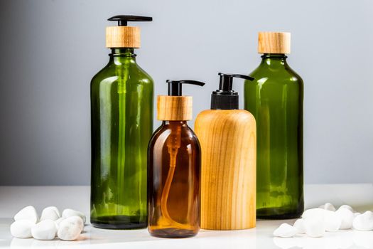 Set of green and brown glass cosmetic bottles with pumps and wooden elements for beauty products refill. Minimalistic bathroom accessories
