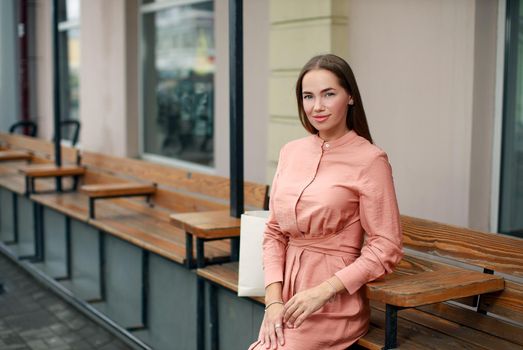 Beautiful girl wearing stylish pink dress sitting on the bench