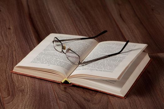 The opened book with glasses on it on wooden background