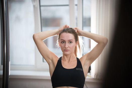 Young attractive woman in sport bra in training studio making a ponytail. Portrait