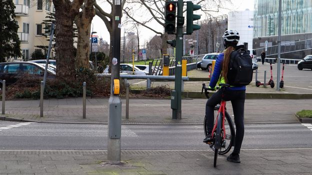 Germany, Dusseldorf - February 28, 2020: A young girl a cyclist in a helmet, stopped at a traffic light and waiting for a permission signal to cross the street. City view
