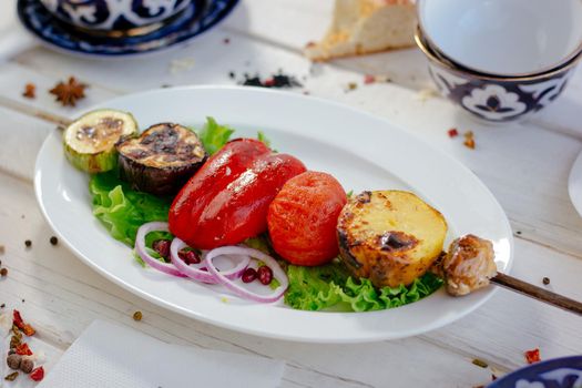 Grilled vegetables - potato, tomato, bell pepper, eggplant and zuccini on skewer over a white plate, great image for your needs.