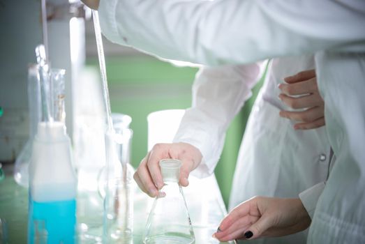 Chemical laboratory. Two young woman holding a flask. Hands in focus