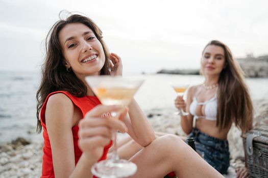 Two young female friends having a picnic on a beach drinking cocktails