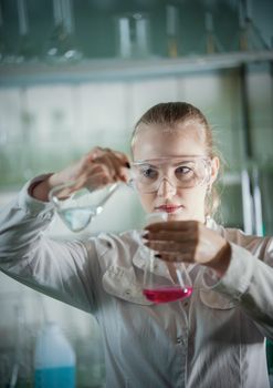 Chemical laboratory. Young blonde woman holding two flasks with liquid in it. Portrait