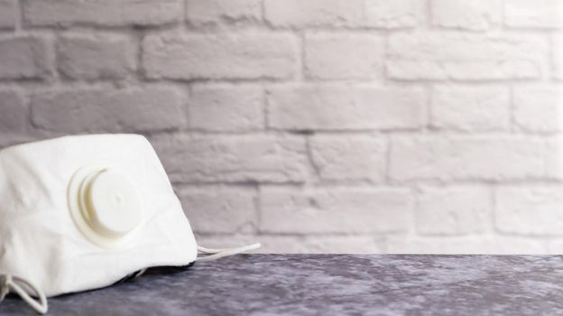 White face shield with flap on a gray table against a white brick wall with copy space. medical masks during outbreaks of viral diseases such as coronavirus or COVID-19 pandemic