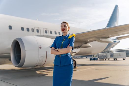 Beautiful stewardess crossed her arms with white plane on the background