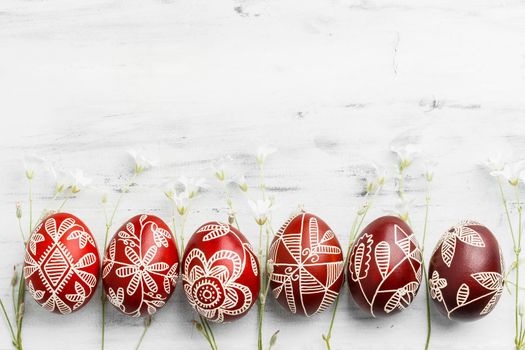 Row of red and white handmade wax dyed Easter eggs. Ukrainian pysanka frame on white wooden background with copy space for text
