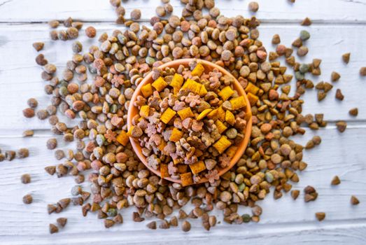 Top view of natural pet food in a clay bowl on white table.
