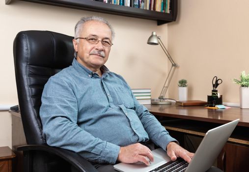 Senior businessman work at home. An elderly man in glasses is working remotely using a laptop. Remote work during coronovirus concept